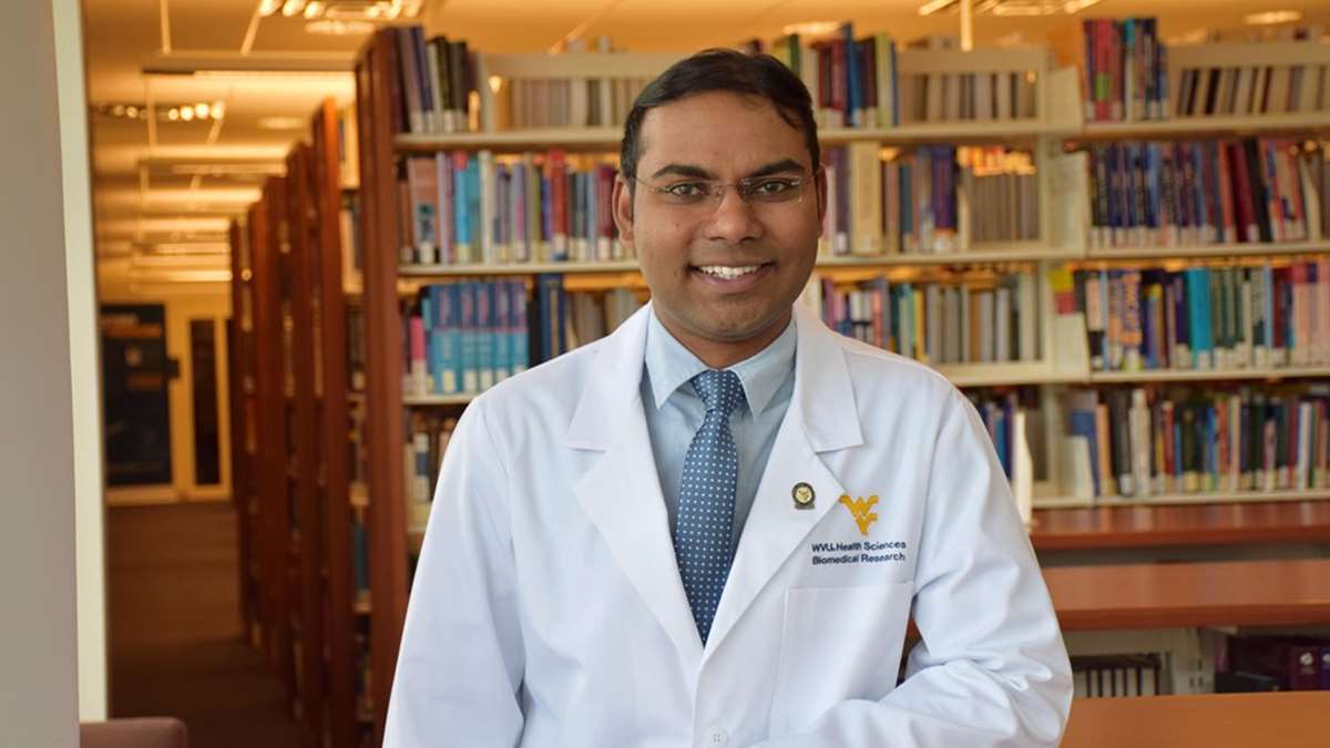 Afroz Mohammad standing in his white coat in front of shelves of books at the library.