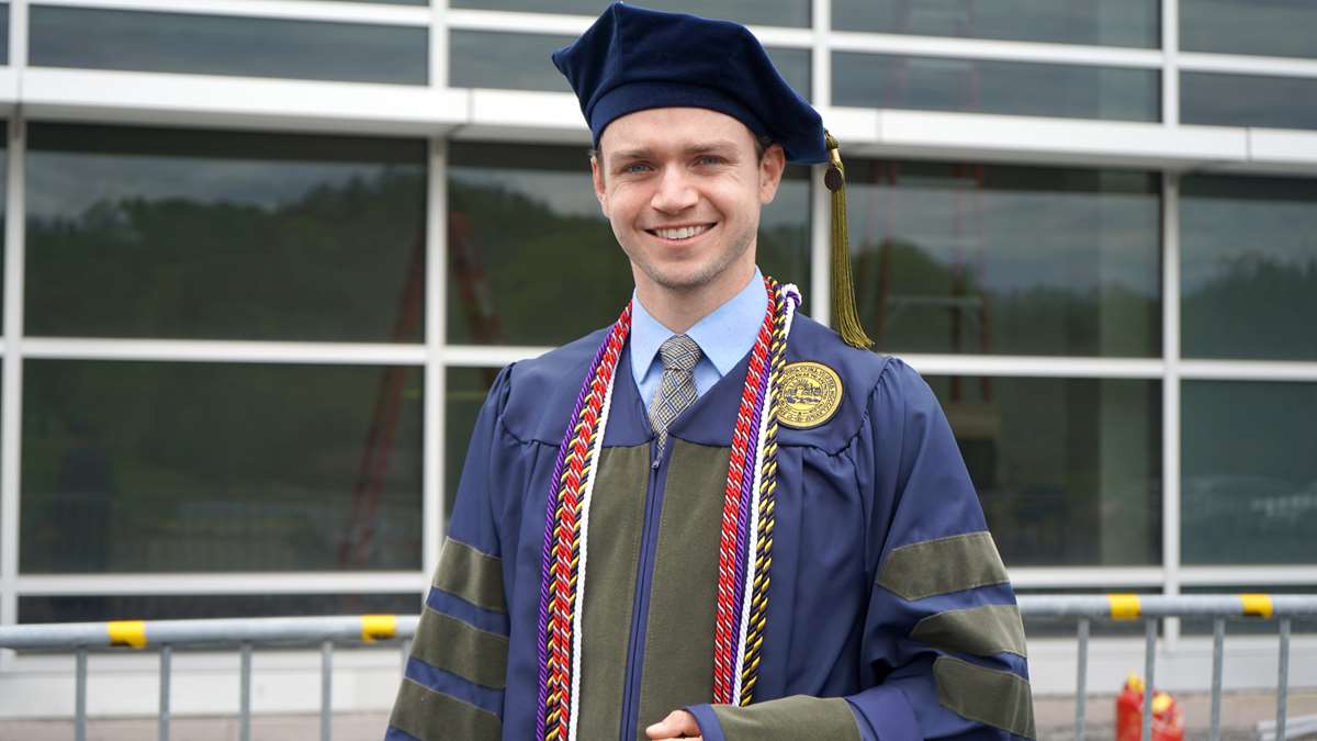 A male pharmacy graduate stands in his cap and gown.
