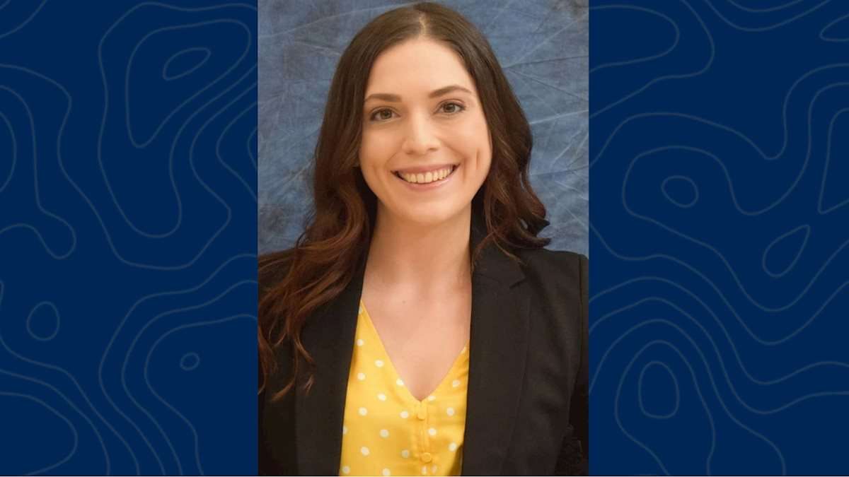 A photo of a female student with brown hair, a black jacket and a yellow shirt.
