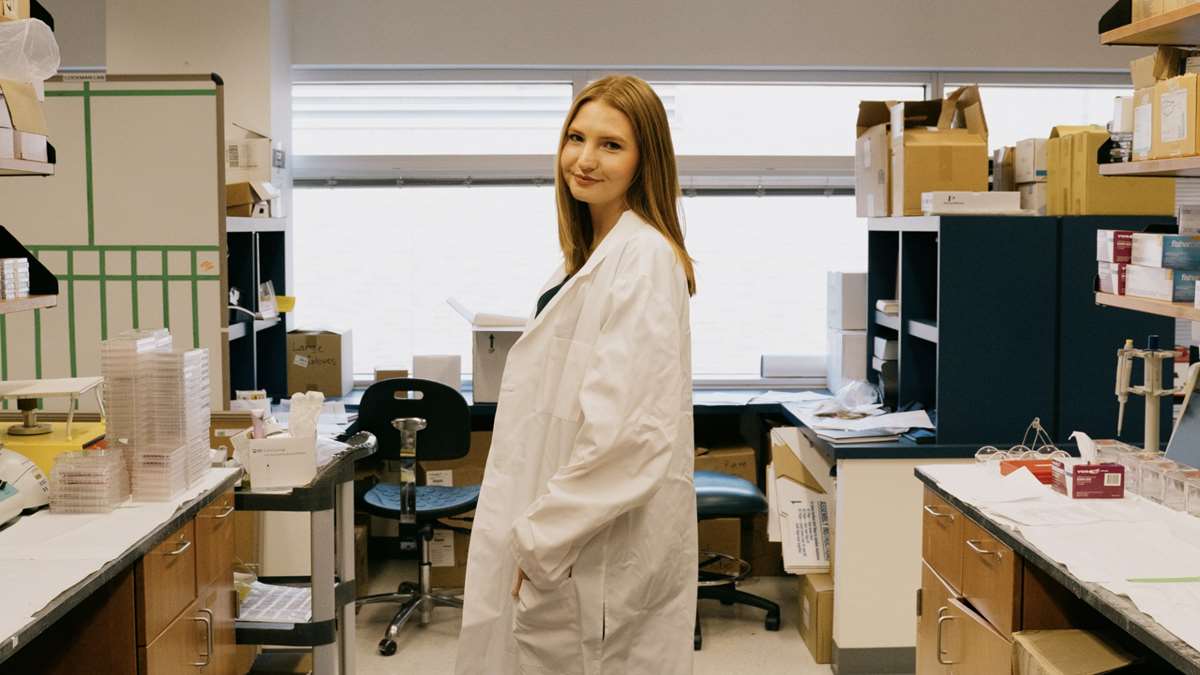 Female in a white lab coat poses in a lab.
