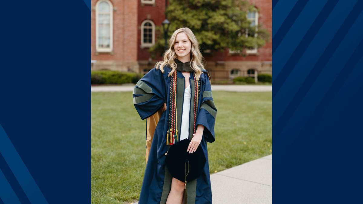 A female in blue commencement regalia poses outside.